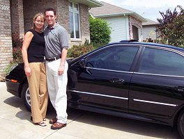 Tim and Heather in front of their car and house